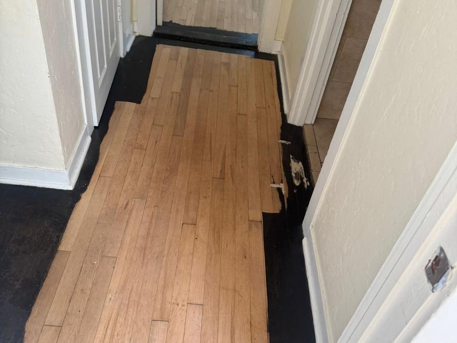 Hallway floor half sanded, black finish removed to reveal oak